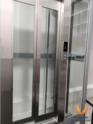 Thang máy quan sát QS07 nhìn từ mặt tầng G với cửa inox và giếng kính khung màu bạc