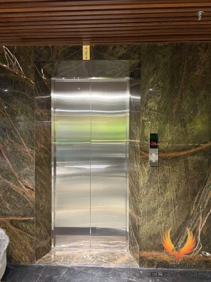 Cửa tầng inox sọc của thang máy tải khách TK08 đặt trong khối ốp đá marble xanh rêu