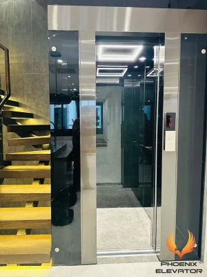 Thang máy quan sát QS08-2026 lắp cạnh cầu thang gỗ, giếng thang vách kính tối màu bắt bulong khung inox sáng