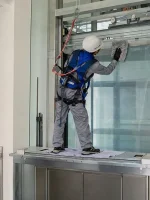 Kỹ thuật viên đeo dây an toàn kiểm tra thiết bị trên nóc cabin bên trong giếng thang