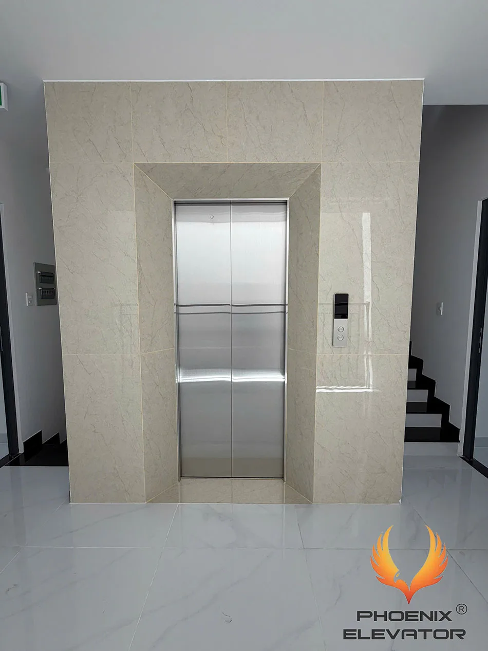 Ô cửa tầng của hố thang máy gia đình sau khi hoàn thiện ốp đá, lắp cửa inox mở trung tâm