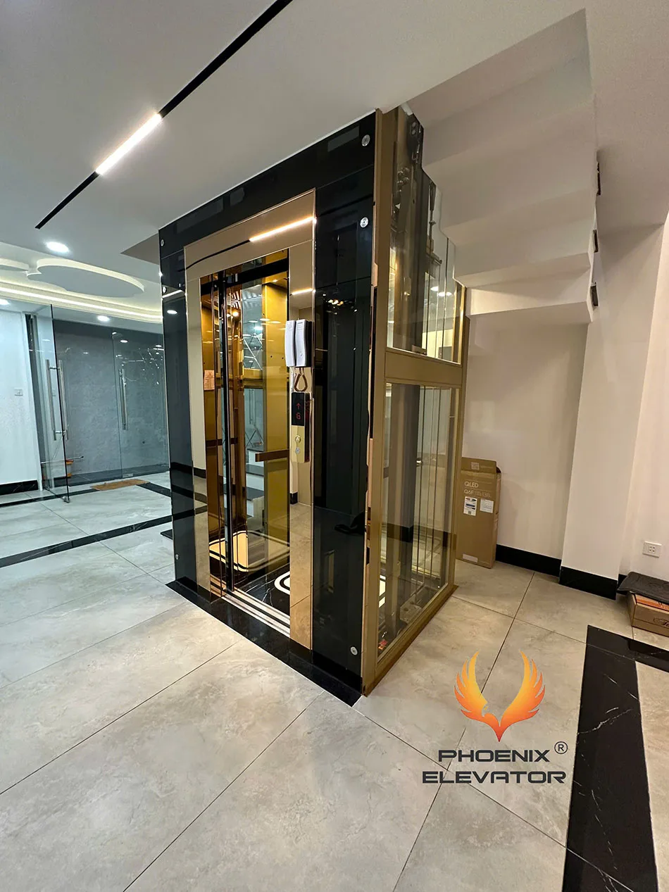 Thang máy quan sát Phụng Hoàng mẫu QS12-2026 khung nhôm vàng đồng, cửa cabin inox mạ vàng đang mở tại nhà phố