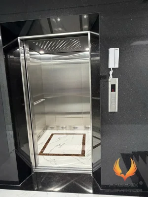 Thang máy tải khách Phụng Hoàng mẫu TK09 cửa tầng mở nhìn vào cabin inox sọc, khối ốp đá granite đen bao cửa